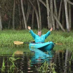 A person on a river in a kayak with her arms raised in the air in triumph. 