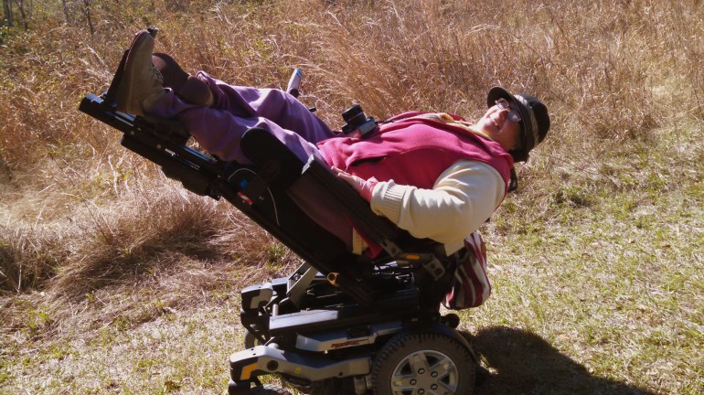 A woman out on a trail with her power chair in tilted and feet raised high position.